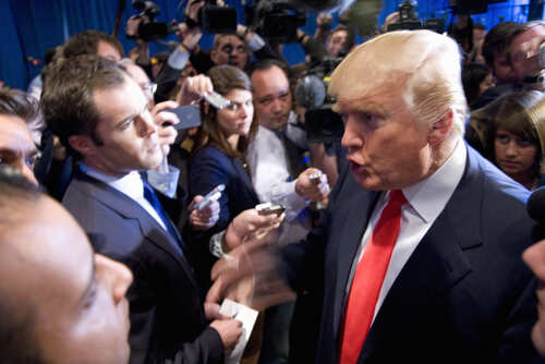 shutterstock_104302025.jpg A man in a suit speaking passionately surrounded by cameras and reporters