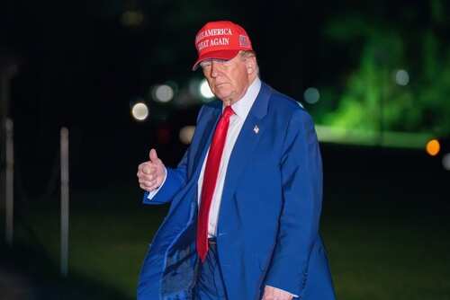 shutterstock_2620657023 (1).jpg A man in a blue suit and red cap giving a thumbs up at night