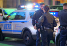 Police officers standing near NYPD vehicles at night
