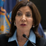 Hochul Under Fire After Supporting Radical Anti-Cop Candidate in Mayoral Race Woman speaking at a podium with flags behind