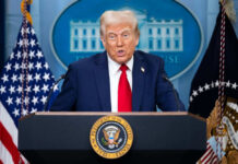 Person speaking at a podium with flags behind