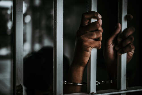 Hands gripping prison bars, suggesting confinement