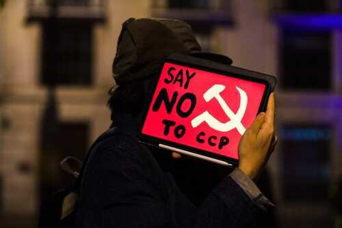 Protester holding a sign that says 'Say No to CCP' with a hammer and sickle symbol