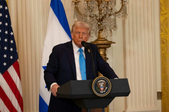 Man speaking at a podium with flags behind him