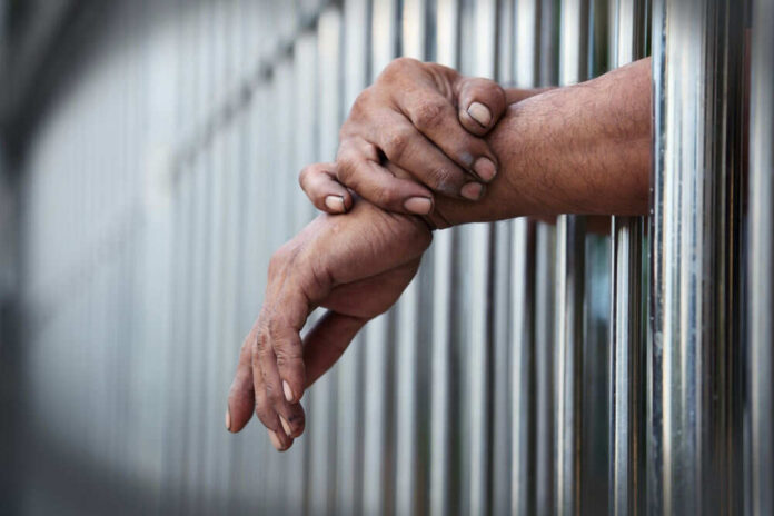 Hands gripping metal prison bars closeup