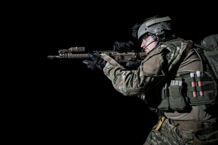 Soldier aiming rifle in tactical gear against black background