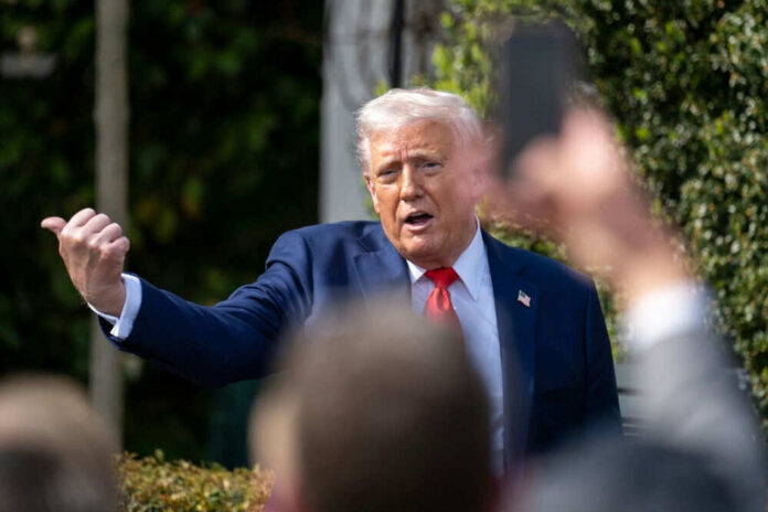 Man in suit gesturing outdoors surrounded by people
