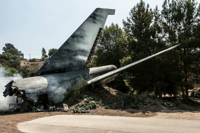 Plane wreckage in wooded area with smoke rising