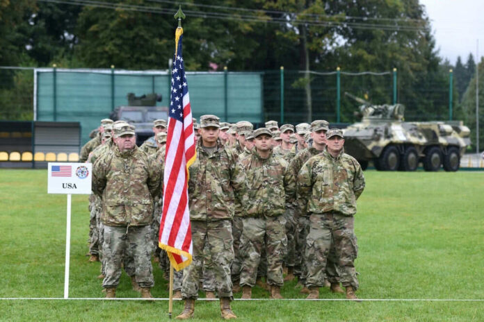 Soldiers in uniform standing with United States flag