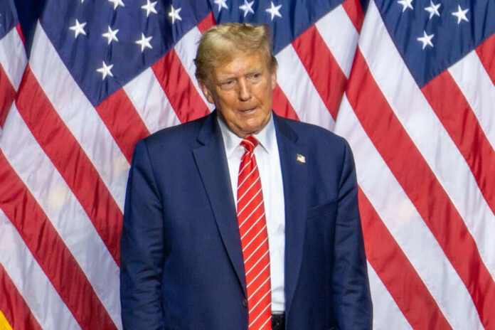 Man in suit standing before American flags