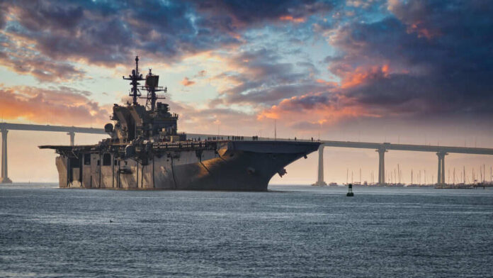 Aircraft carrier near bridge under colorful sunset sky
