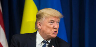 Man in suit speaking with flags in background